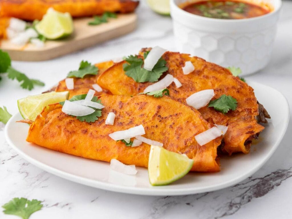 Two quesabirria tacos with orange-red shells, topped with chopped onions and cilantro.