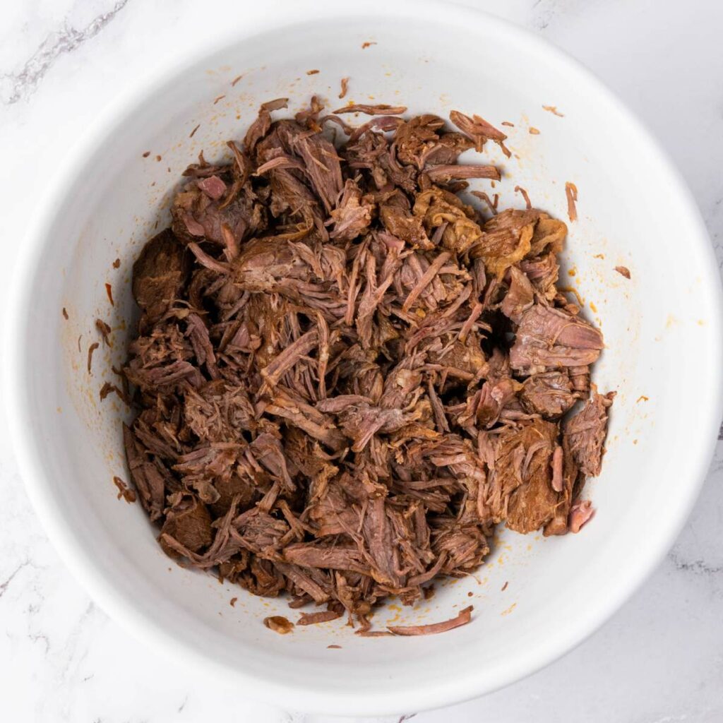 Shredded cooked beef in a white bowl.