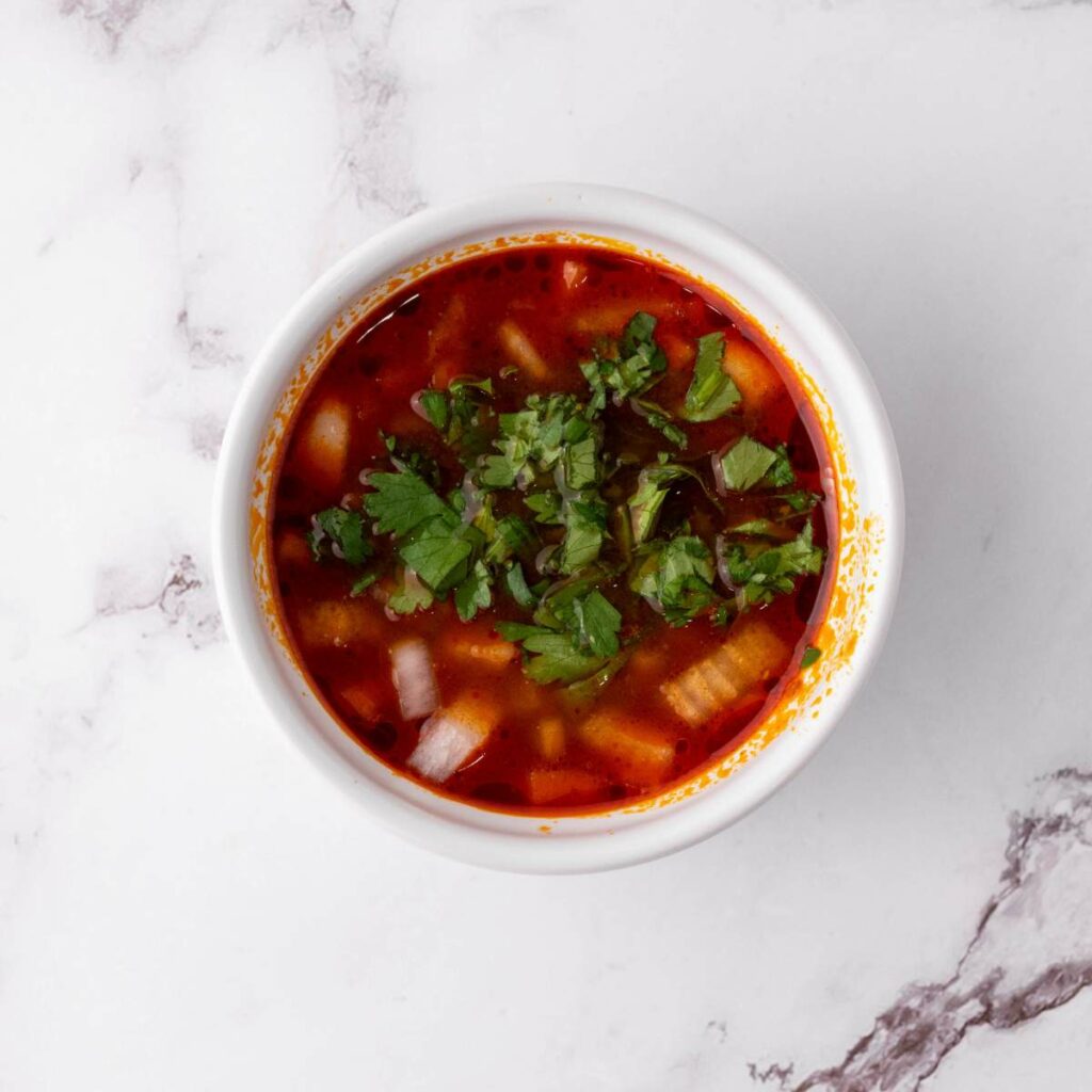 A bowl of red soup topped with chopped onions and cilantro.