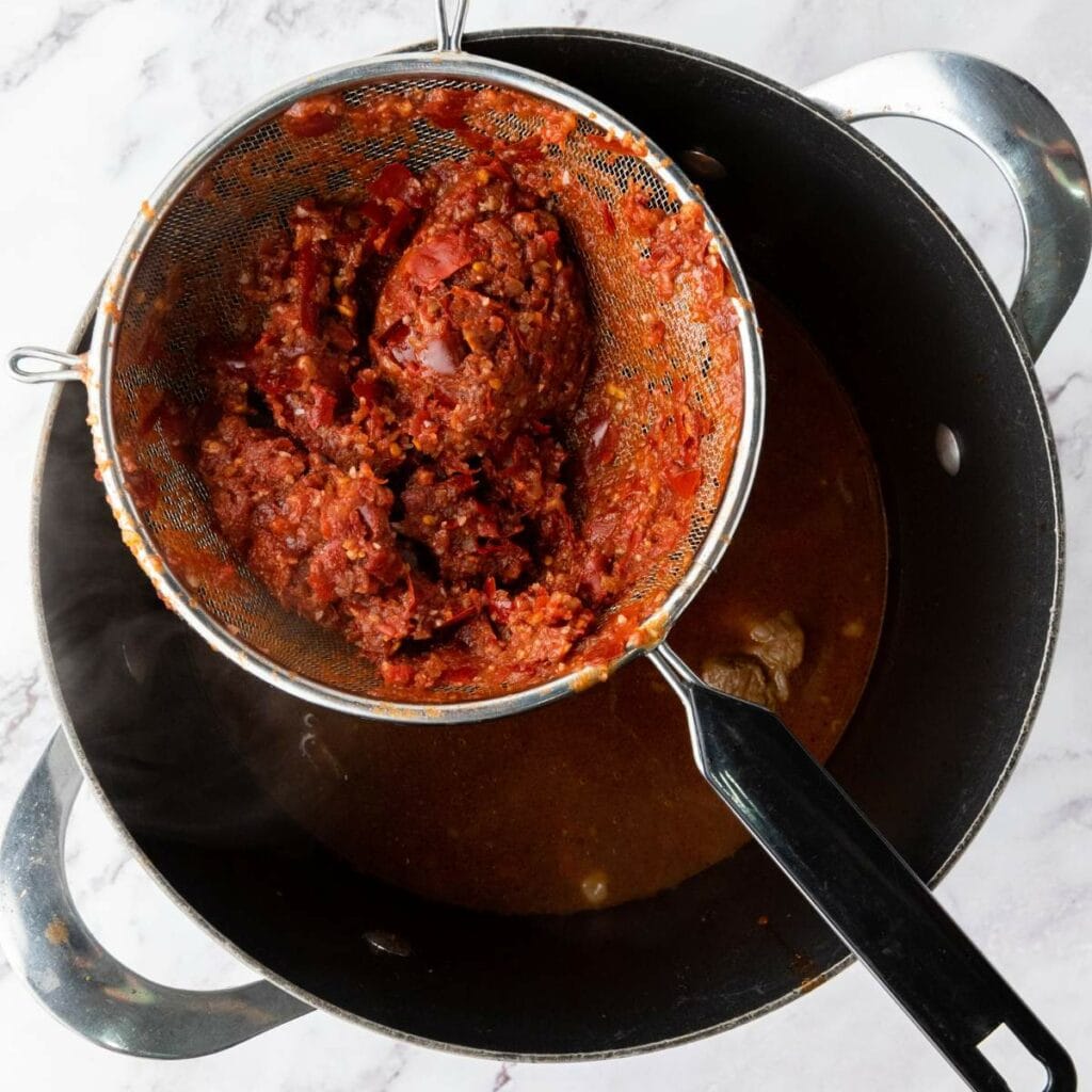 A metal strainer with tomato paste.