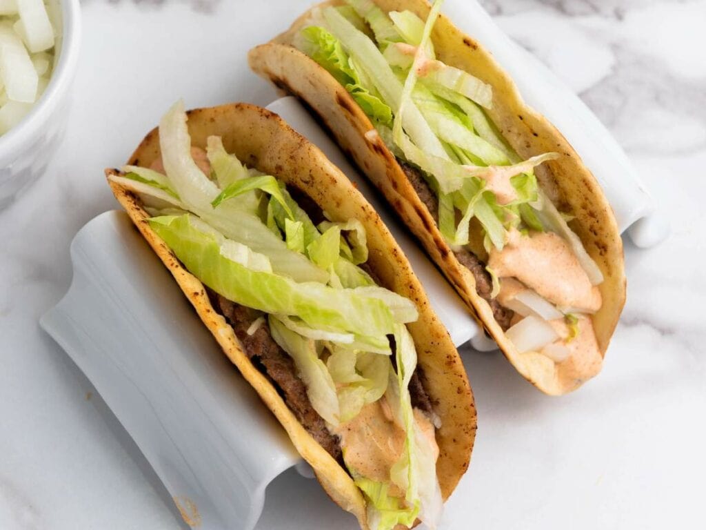 Smash burger taco filled with ground beef, shredded lettuce, diced onions, and a creamy sauce.