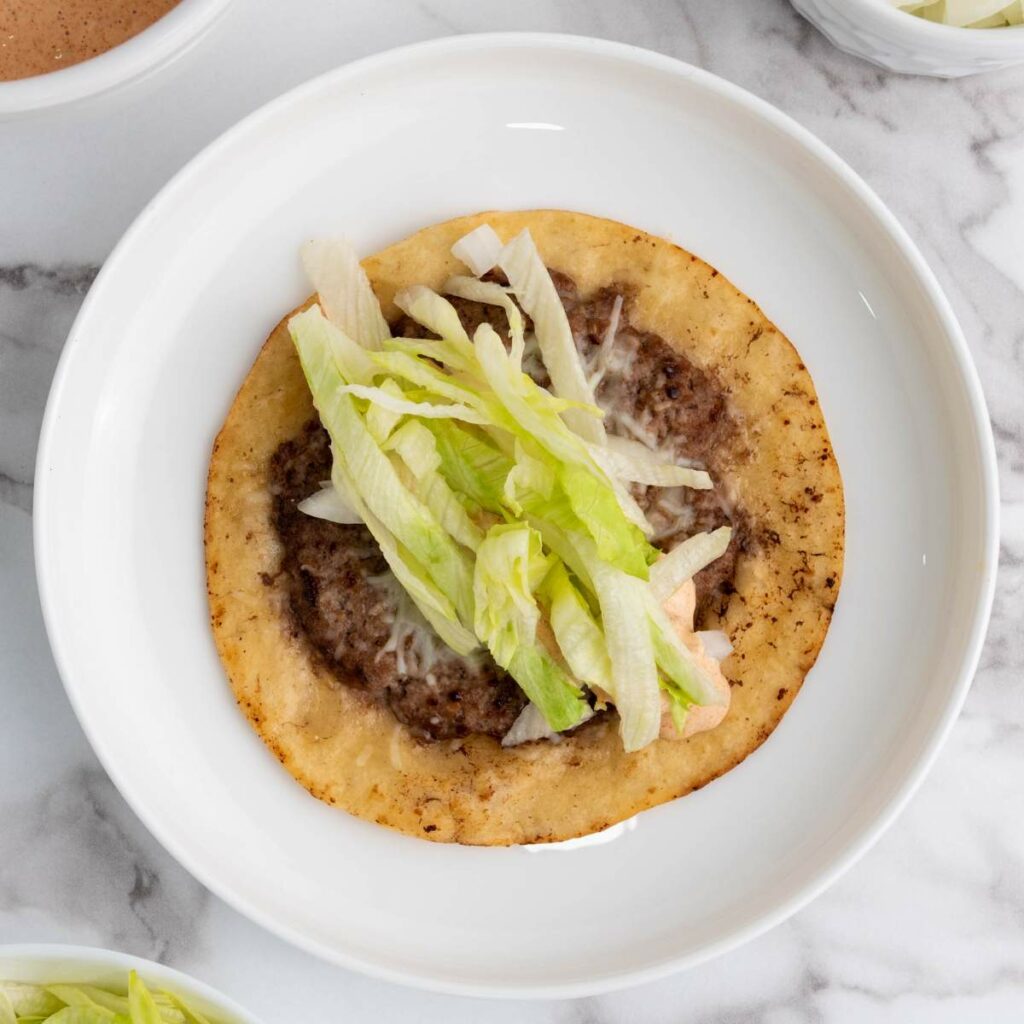 A tostada topped with ground beef, melted cheese, and shredded lettuce.