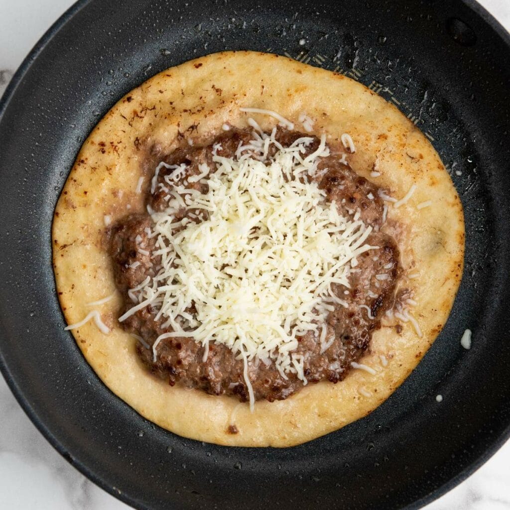 A round flatbread topped with refried beans and shredded cheese.