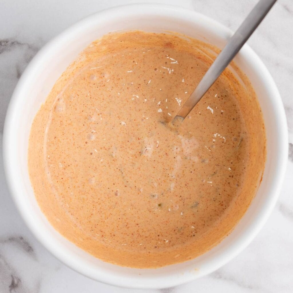 A white bowl filled with a creamy, orange-colored sauce or dip.