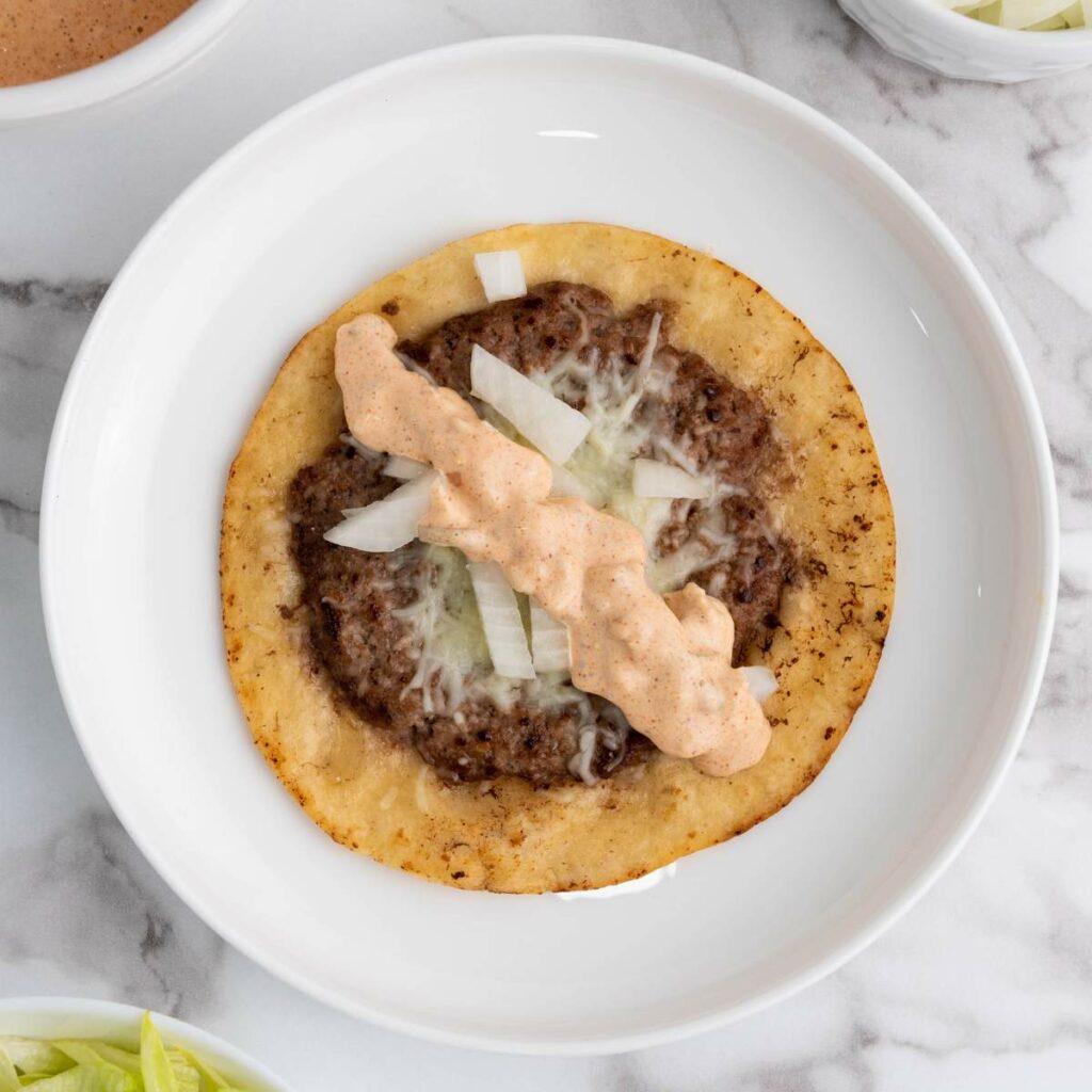 A tortilla with ground beef, shredded cheese, chopped onions, and a drizzle of creamy sauce.