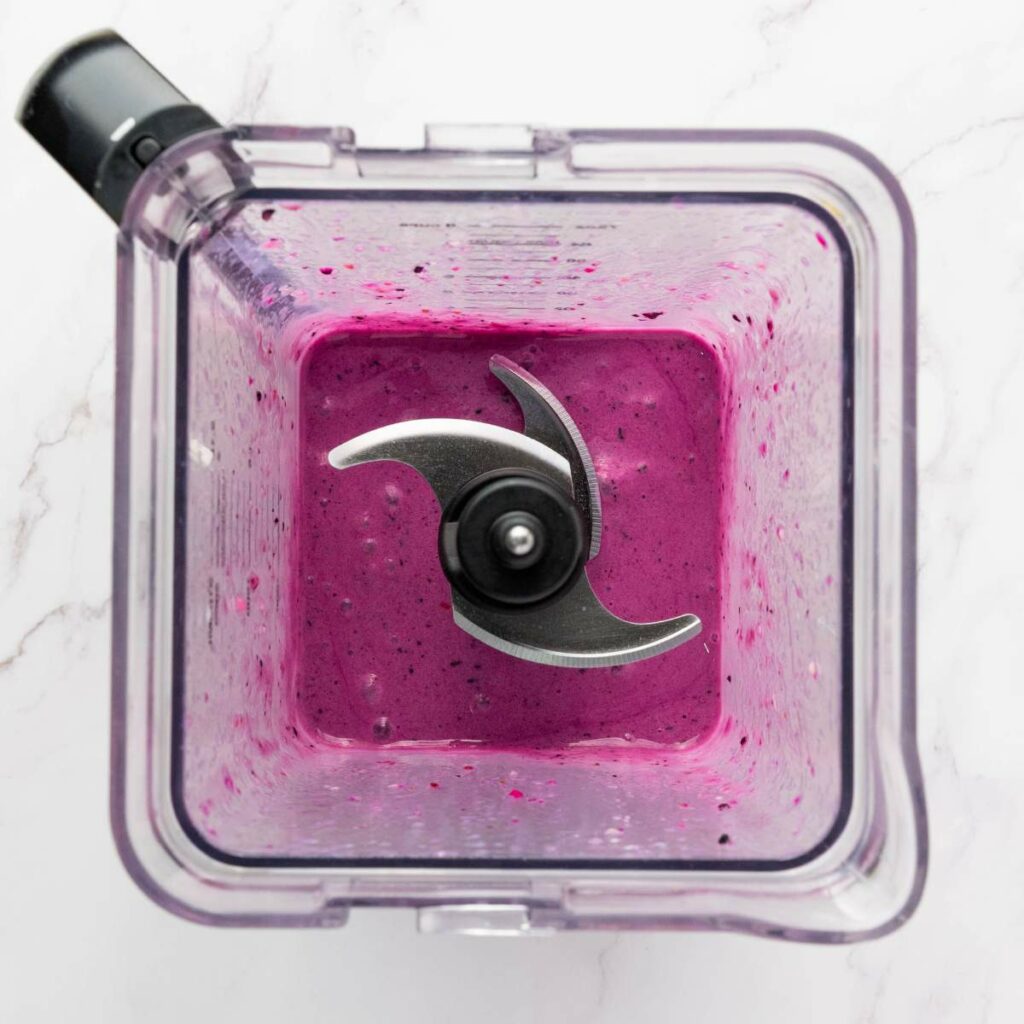 Overhead view of a blender containing a thick, purple smoothie with the blades visible in the center.