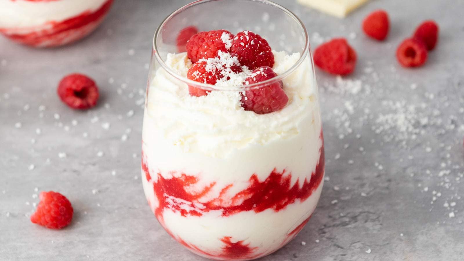 White chocolate mousse of layered raspberry and cream dessert, topped with whole raspberries and white chocolate shavings.