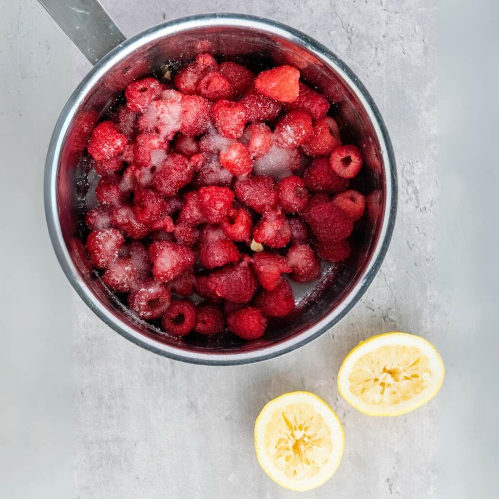 A metal pot filled with frozen raspberries and sugar.
