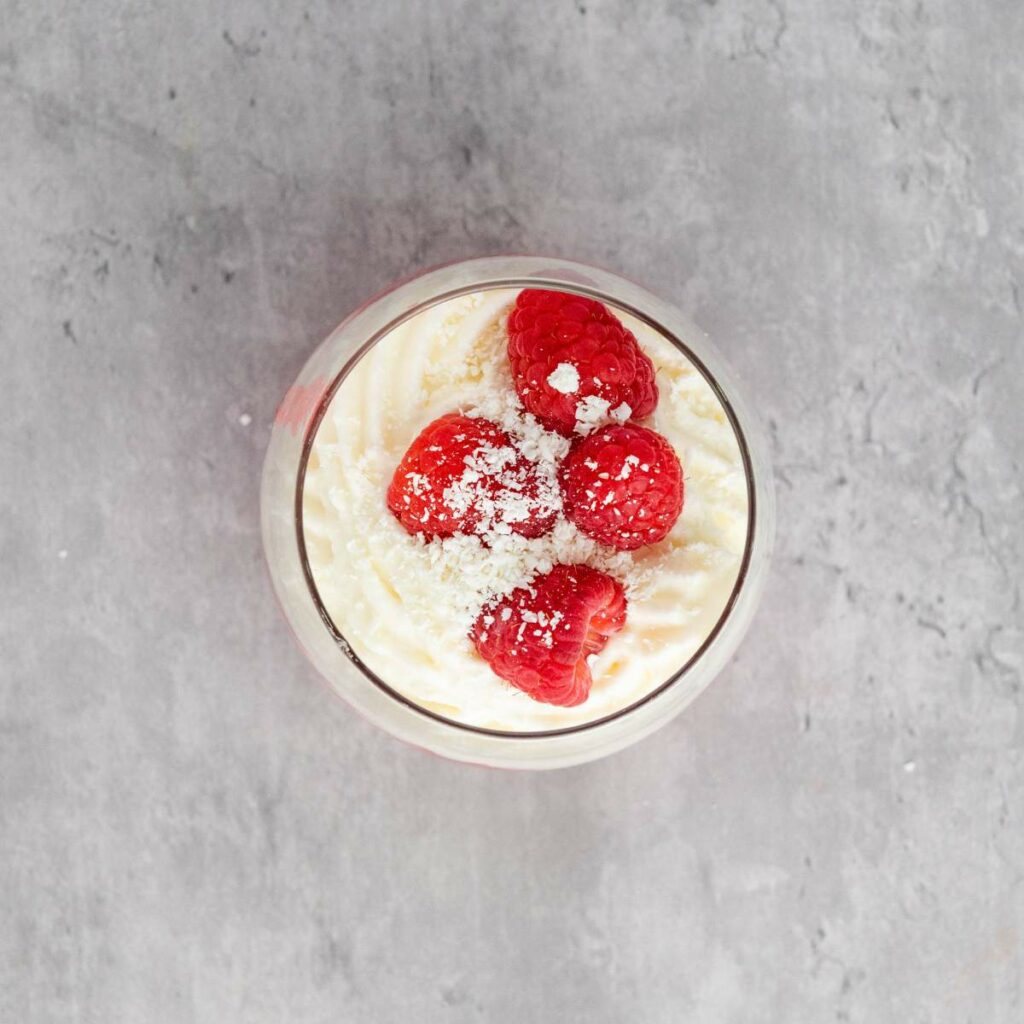 A glass filled with creamy dessert topped with three raspberries.