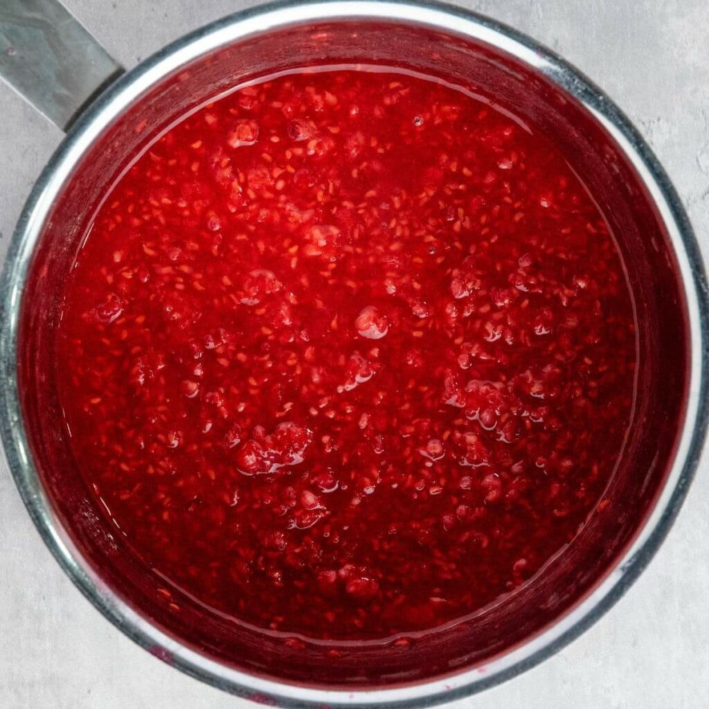 A pot filled with raspberry sauce or compote, showing a vibrant red color and visible fruit seeds.