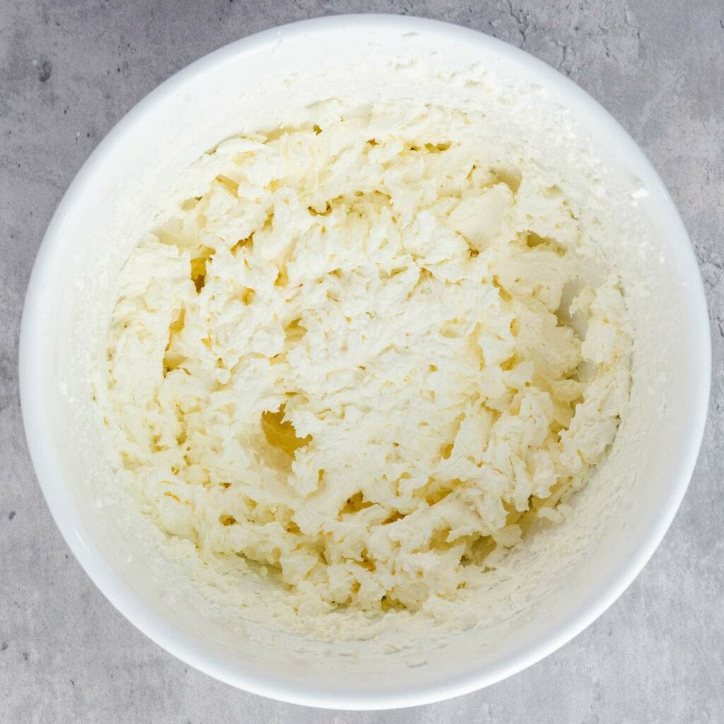 A white mixing bowl containing creamed butter and sugar mixture.