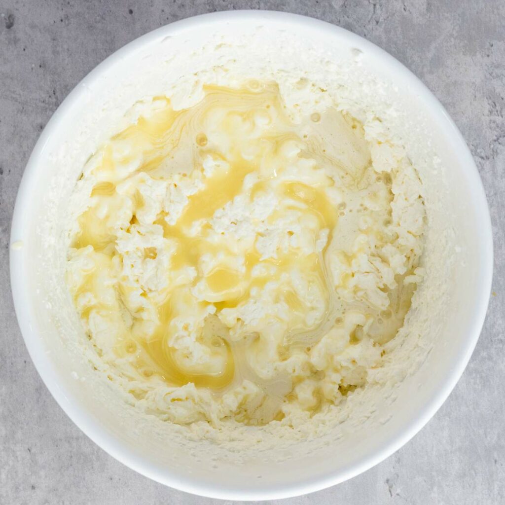 A white bowl containing a mixture of mashed potatoes and melted butter.