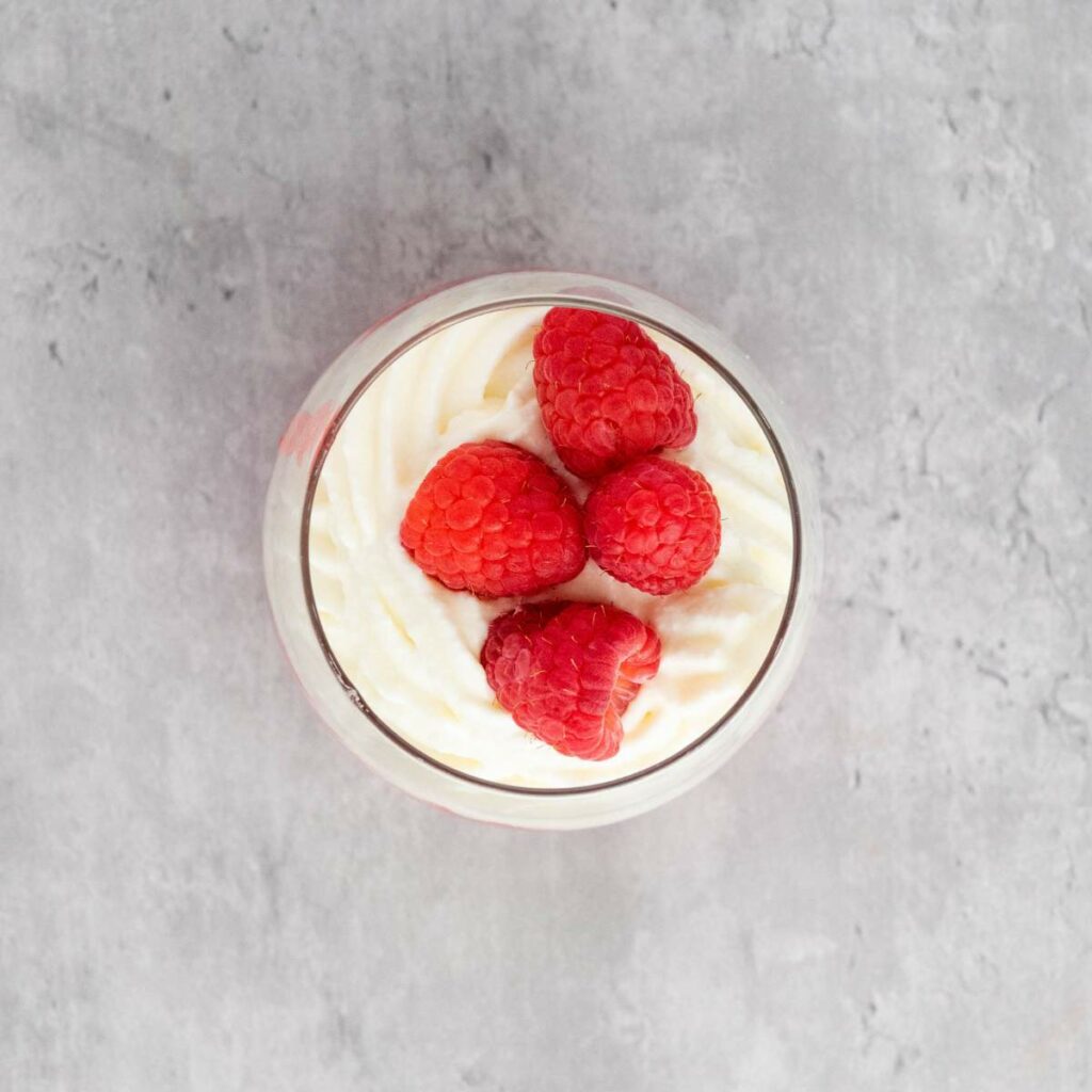 A glass filled with swirled whipped cream topped with four fresh raspberries.