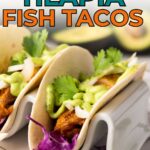 Two blackened tilapia fish tacos topped with cilantro, onions, and green sauce, served in soft tortillas with purple cabbage in a white taco holder.