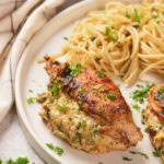 A half look of stuffed chicken breast on a white plate next to a white striped table napkin.