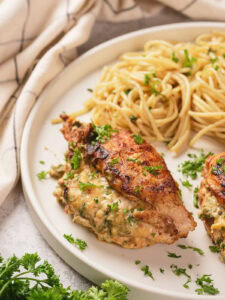 A half look of stuffed chicken breast on a white plate next to a white striped table napkin.