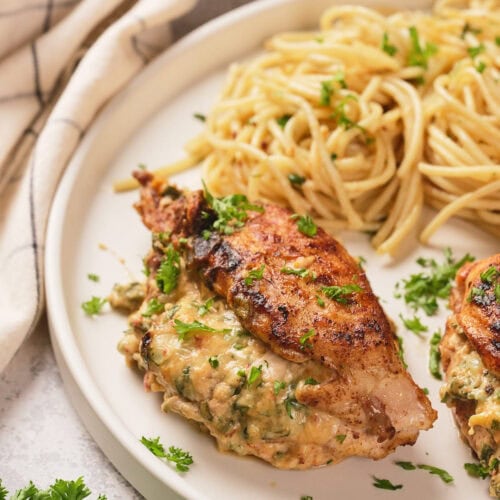 A half look of stuffed chicken breast on a white plate next to a white striped table napkin.