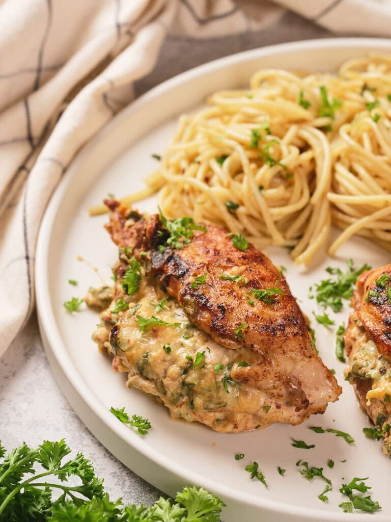 A half look of air fryer stuffed chicken breast on a white plate next to a white striped table napkin.