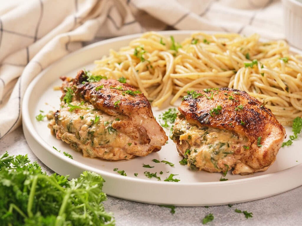 A plate of air fryer stuffed chicken breast garnished with fresh parsley with cooked pasta next to it and white striped cloth.
