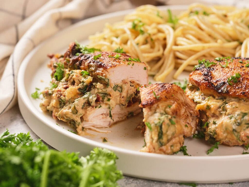 A plate of air fryer stuffed chicken breast sliced on half garnished with parsley on a white plate.