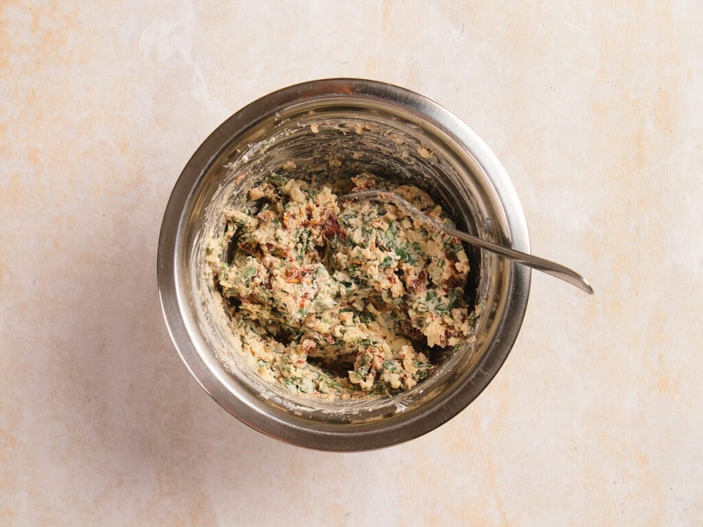 A bowl of mix ingredients for stuffed chicken breast with a metal fork inside on a light surface.