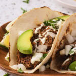 A barbacoa on a fried tortilla on a wooden taco on a light surface.