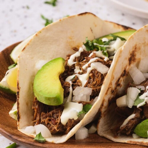 A barbacoa on a fried tortilla on a wooden taco on a light surface.