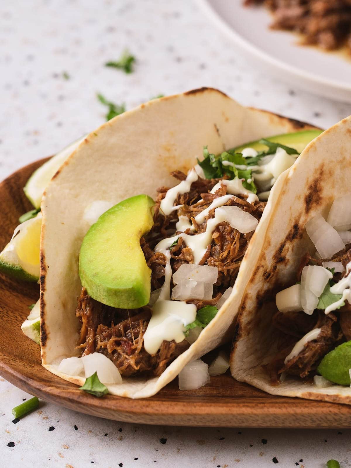 A barbacoa on a fried tortilla on a wooden taco on a light surface.