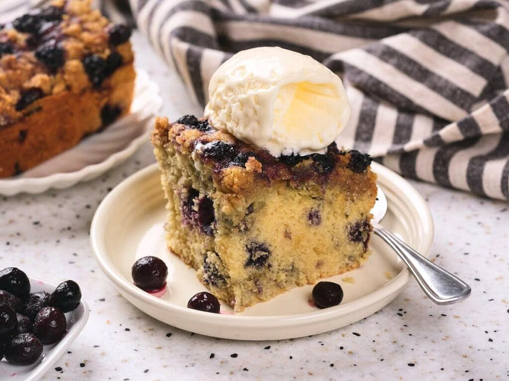 A slice of blueberry buckle topped with a scoop of vanilla ice cream.