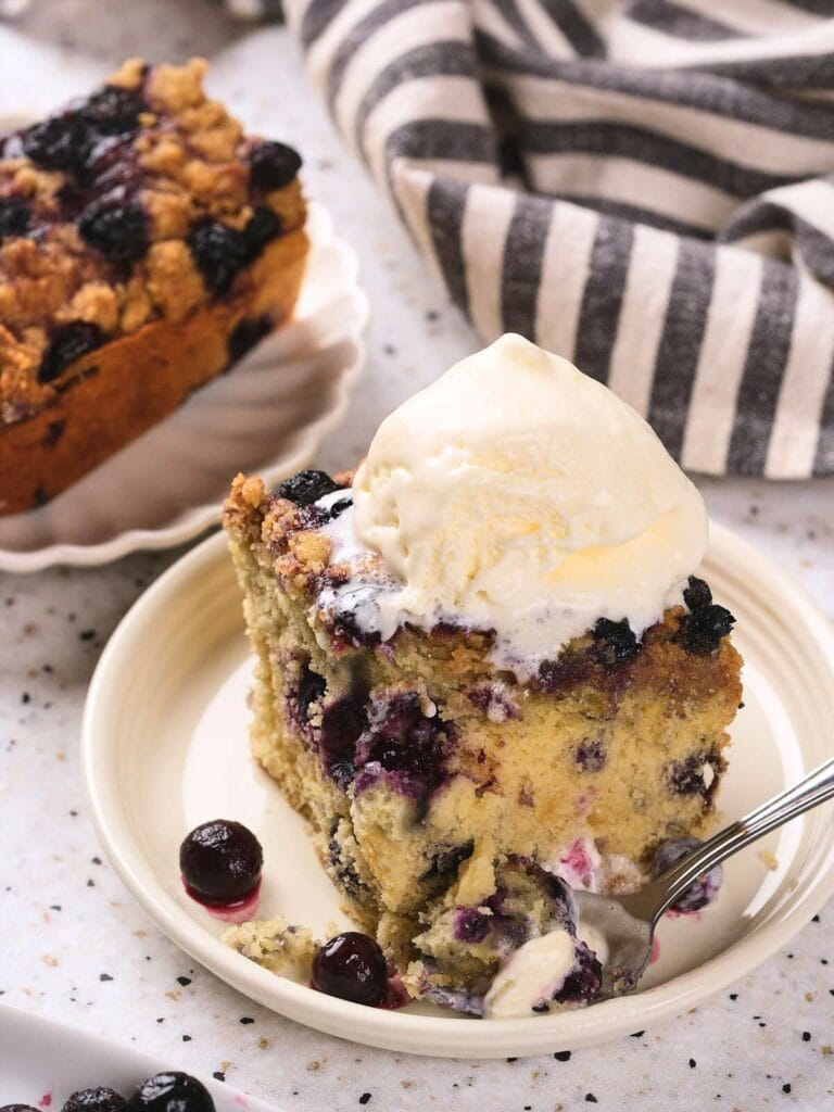 A slice of blueberry buckle topped with a scoop of vanilla ice cream.