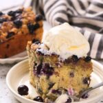 A slice of blueberry buckle topped with a scoop of vanilla ice cream on a plate.