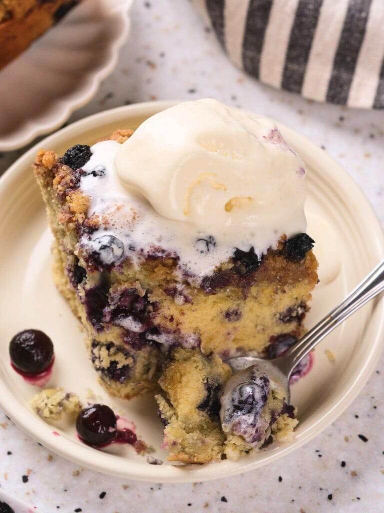 A blueberry buckle topped with a scoop of vanilla ice cream sits on a plate.