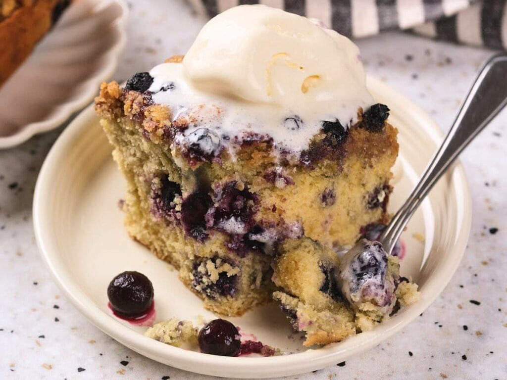 A slice of blueberry buckle topped with melting vanilla ice cream.