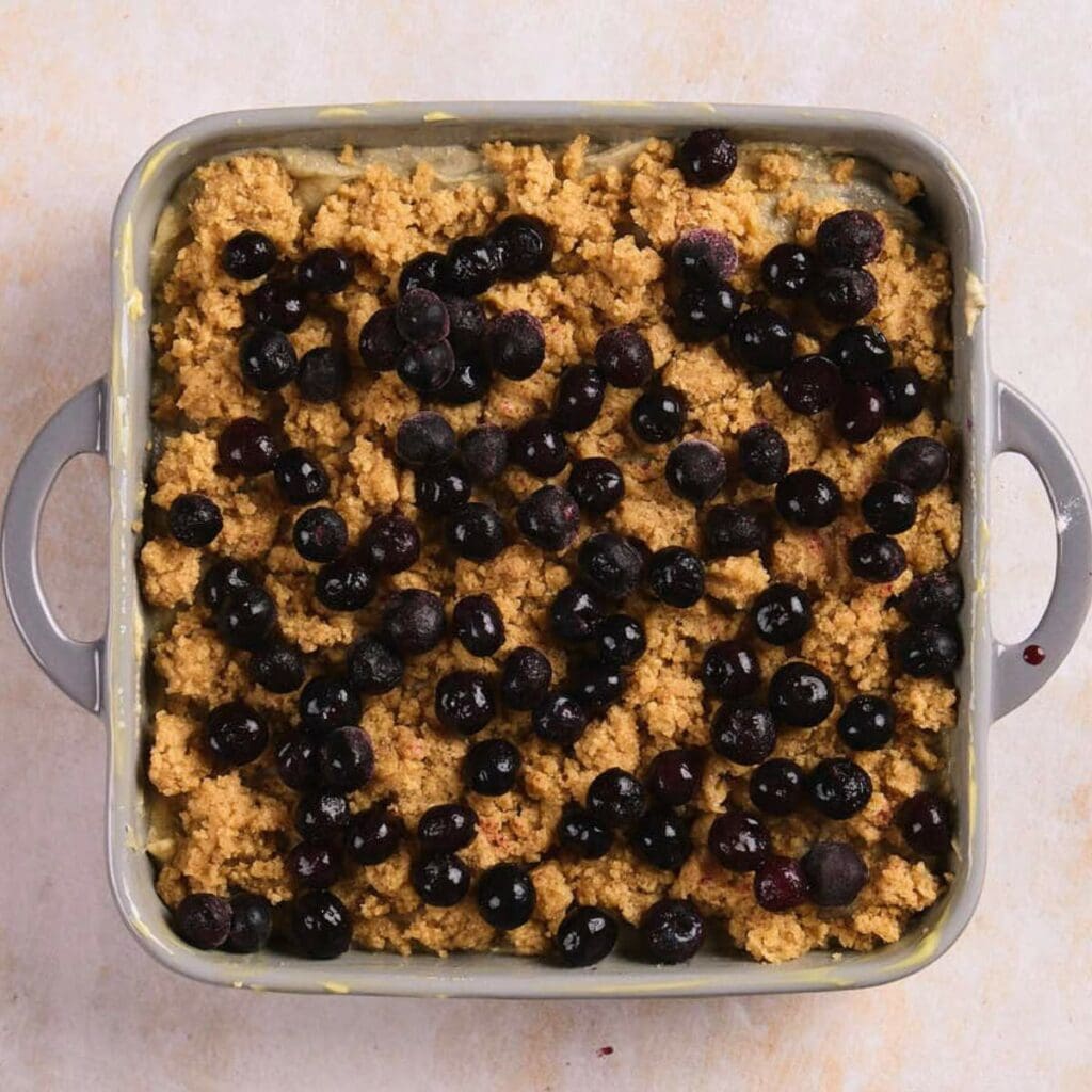 A square baking dish filled with a crumbly dough topping and scattered blueberries.