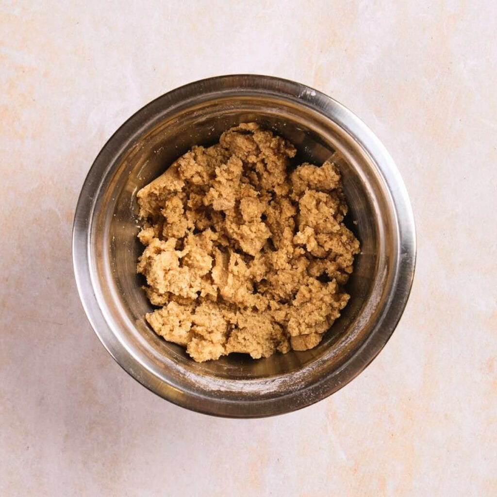 A metal mixing bowl containing a coarse, light brown dough mixture.