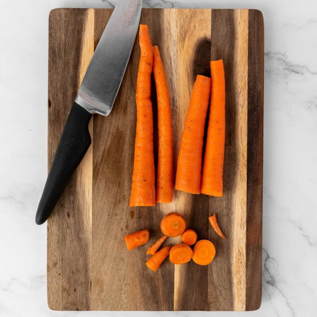 A kitchen knife and carrots are trimmed both sides are placed on a wooden cutting board.