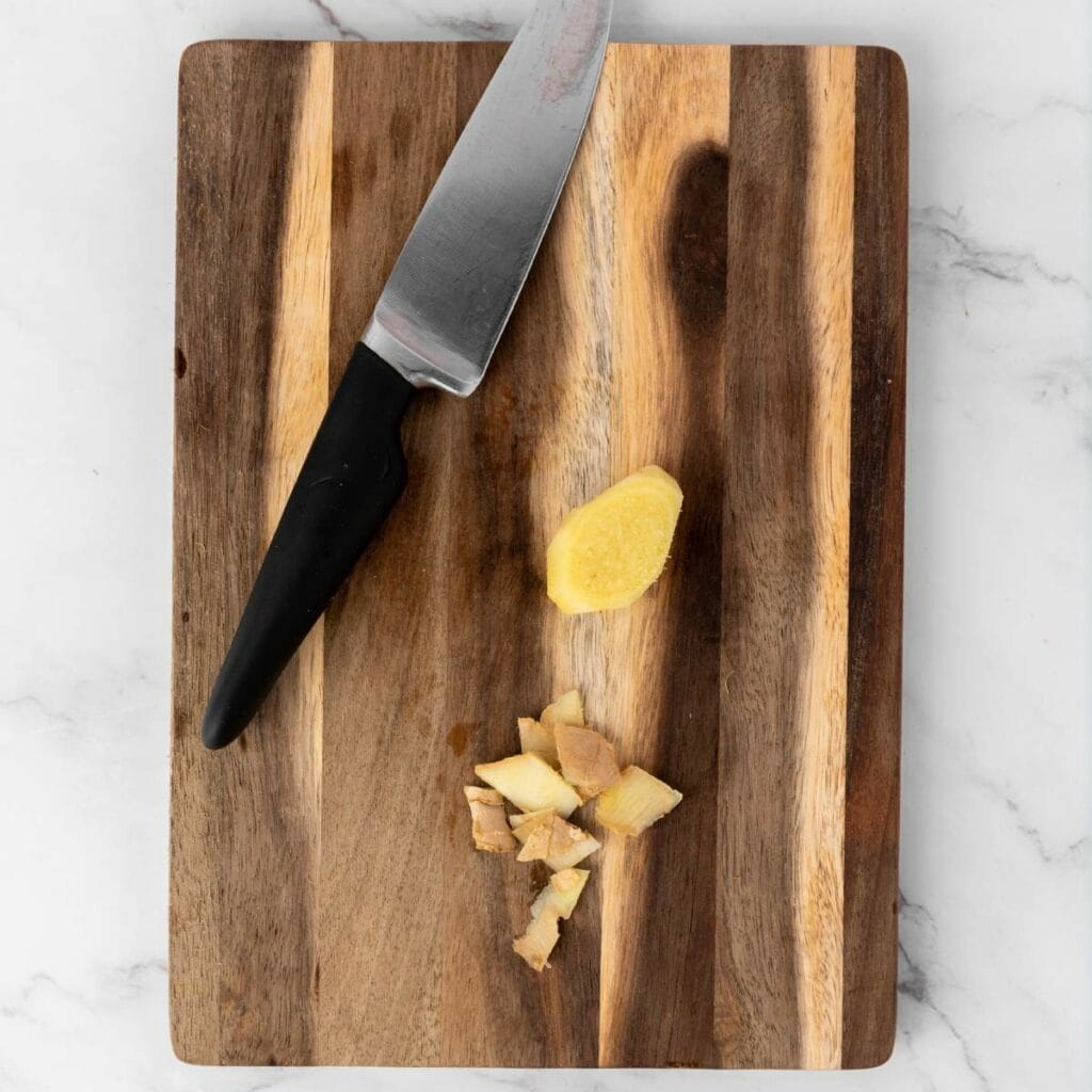 A kitchen knife and chopped pieces of ginger root on a wooden cutting board.
