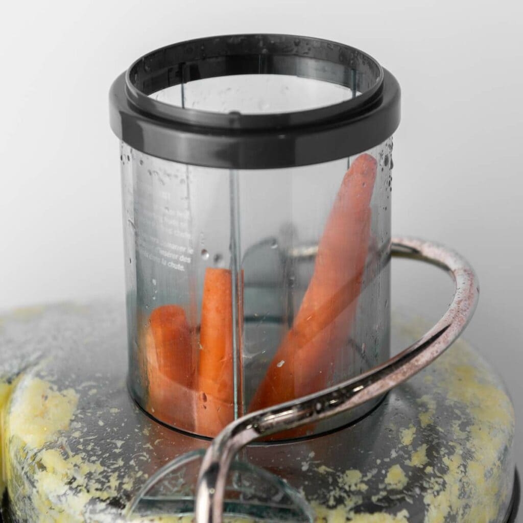 A transparent juicer holding several whole carrots with visible orange and ginger residue.