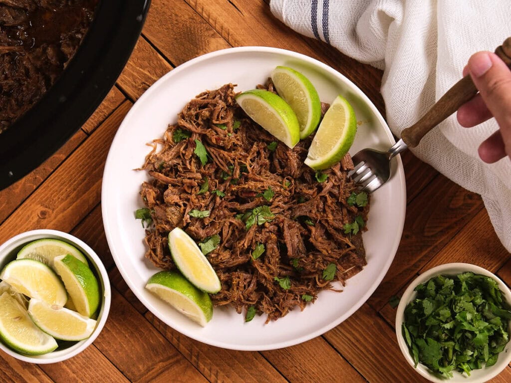 A plate of chipotle barbacoa with a hand holding a fork on a wooden surface.