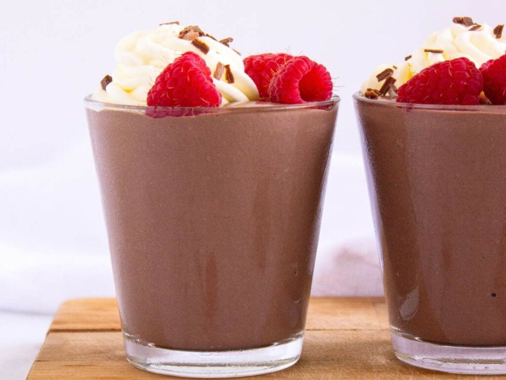 One and one half glasses of chocolate cottage cheese pudding topped with whipped cream, fresh raspberries, and chocolate shavings.