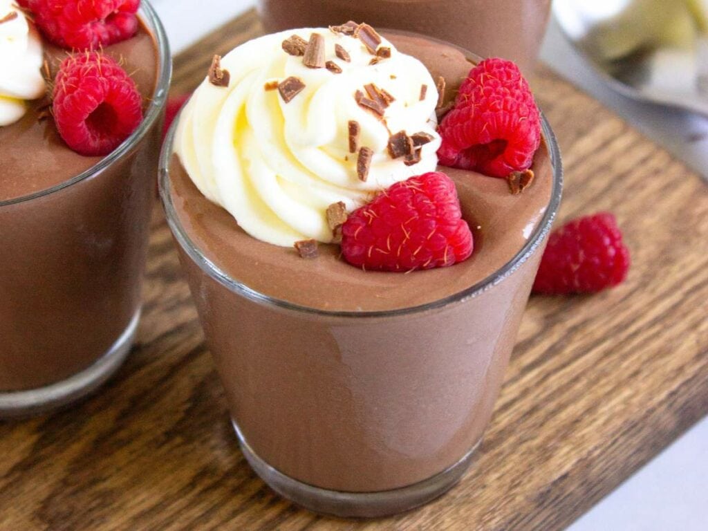 Glass of chocolate cottage cheese pudding with toppings on a cutting board.