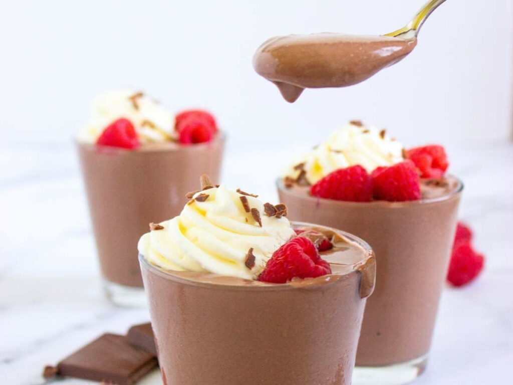 Three glasses of chocolate cottage cheese pudding with toppings and a spoonful of mousse being held above one glass.