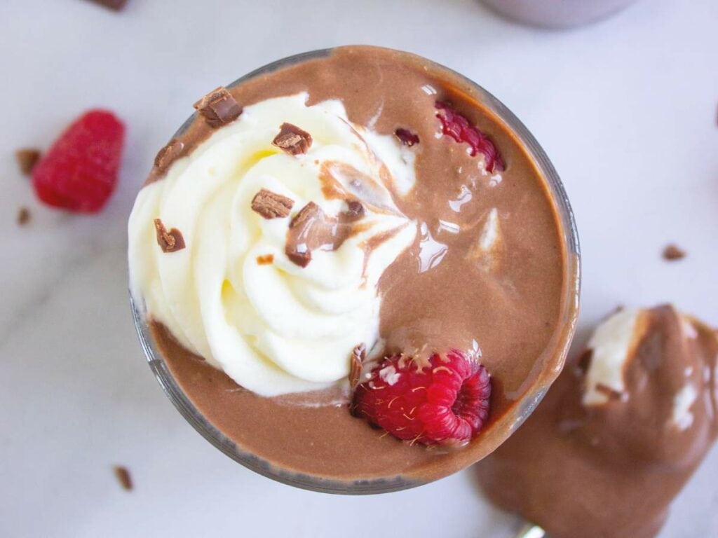 A close-up of a glass filled with chocolate cottage cheese pudding with whipped cream mixing in to pudding.