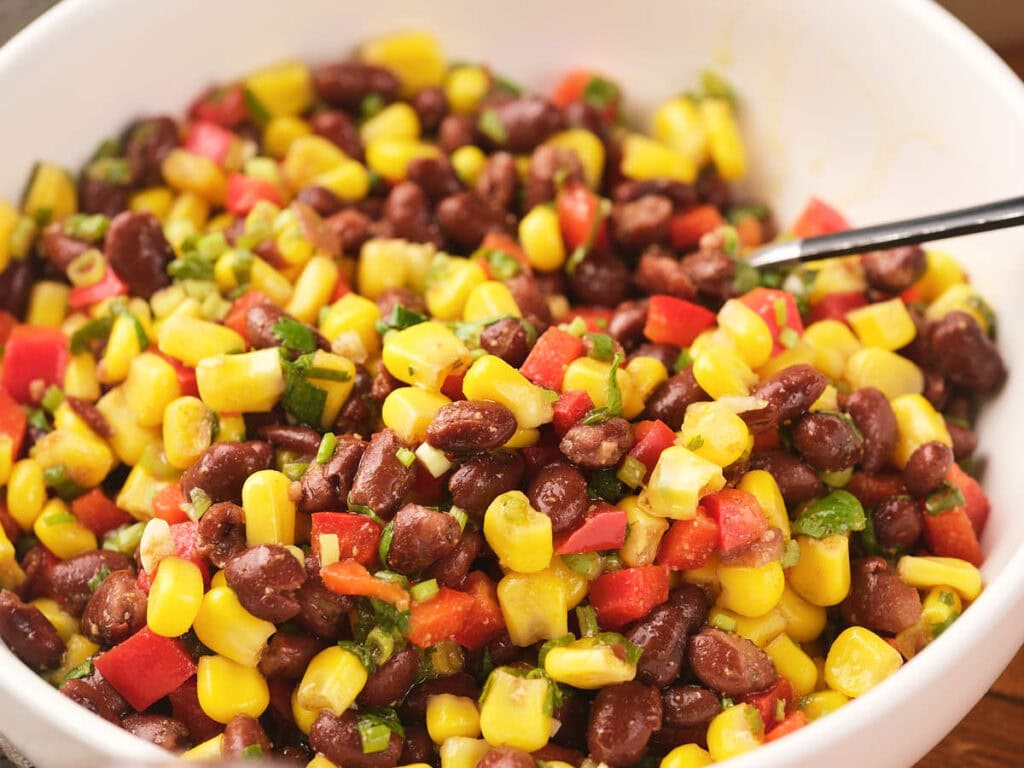 Close-up bowl of corn and black bean salad with a spoon on the right side.