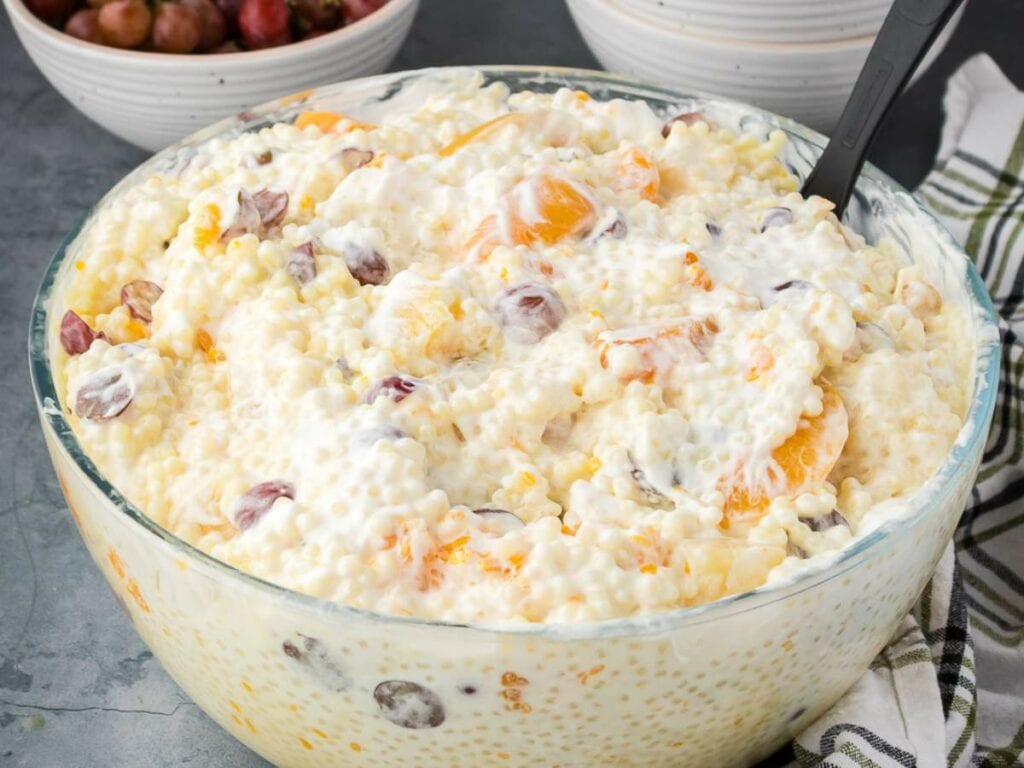 A large glass bowl filled with creamy frog eye salad with a serving spoon inside.