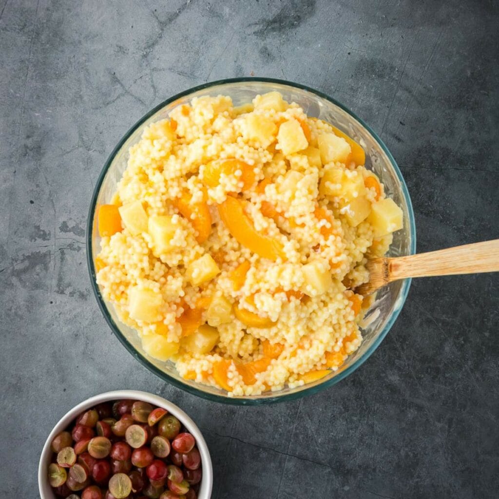 A glass bowl of creamy frog eye salad next to a small bowl of grapes on a gray surface.