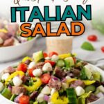 A bowl of Italian salad with cherry tomatoes, mozzarella, cucumbers, red onions, olives, pepperoncini, and salami on a white table.