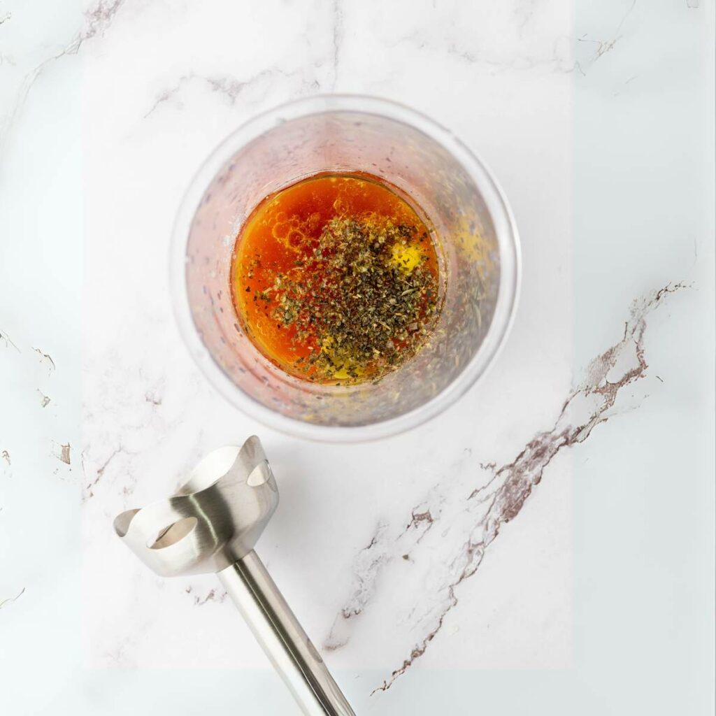 A glass container with oil, spices, and herbs inside.