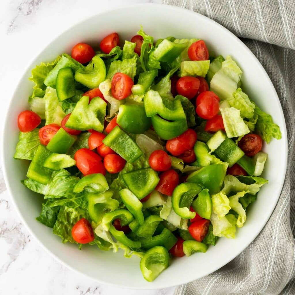 A bowl of salad containing chopped romaine lettuce, green bell peppers, and grape tomatoes.
