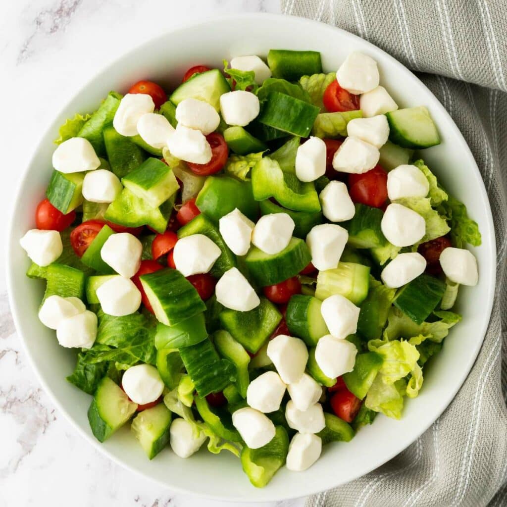 A bowl of salad with cherry tomatoes, cucumber, green bell pepper, lettuce, and mozzarella balls.